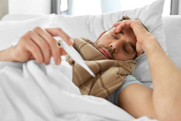Man with fever in bed checking temperature